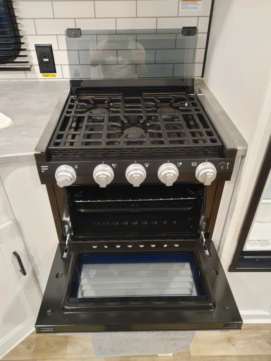 Black gas stove & oven with open door and glass cooktop cover in a modern RV rental kitchen setting.. Keystone RV Hideout 2022