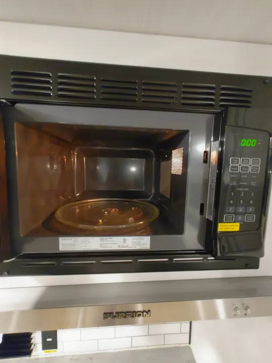 Open black microwave oven with glass turntable and digital display in an RV rental kitchen. Furrion appliance.. Keystone RV Hideout 2022