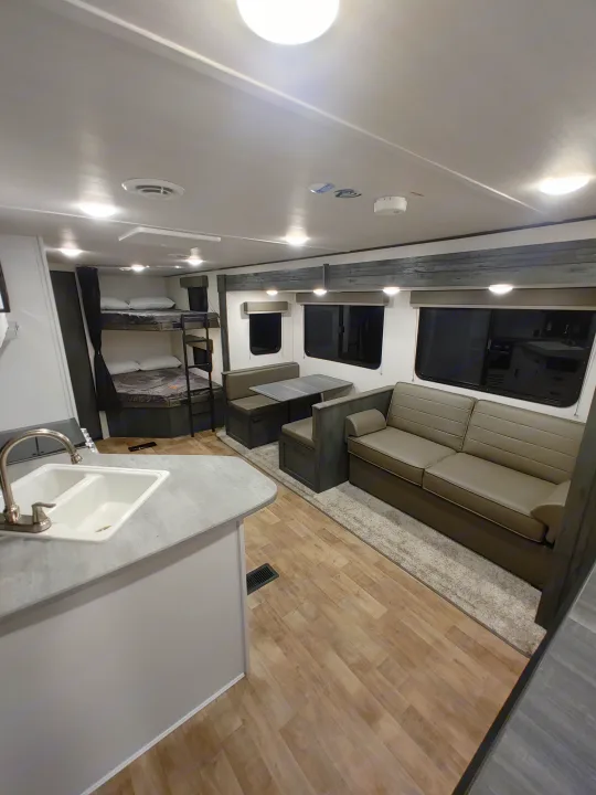 Explore this bright RV rental interior featuring a kitchen sink, bunk beds, a dinette, and a comfy sofa, ideal for travel.. Keystone RV Hideout 2022