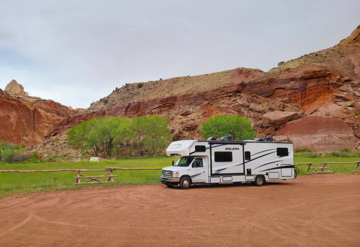 White RV rental on red dirt, backed by green fields & majestic red rock mountains under a cloudy sky.. Forest River Solera 2022
