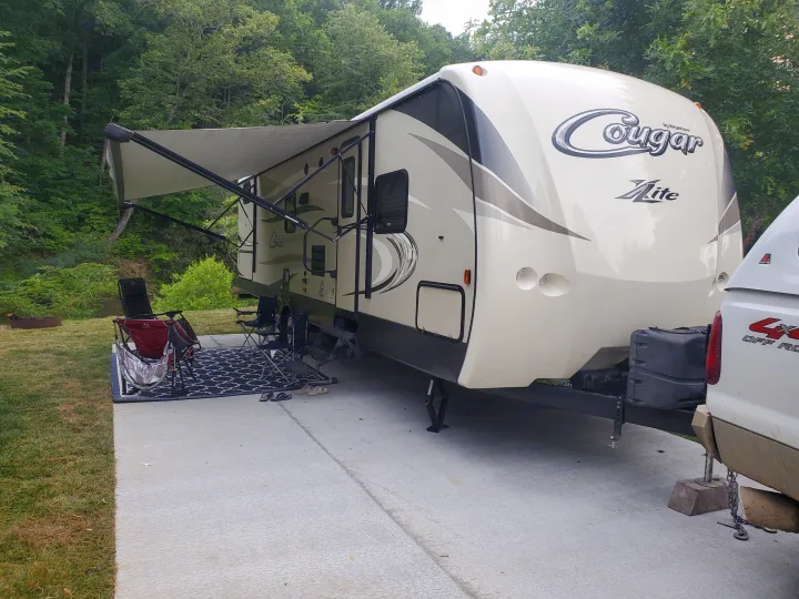 This Cougar Lite travel trailer RV rental is set up at a scenic campsite with an extended awning and outdoor living space.. Keystone Cougar Xlite 2020