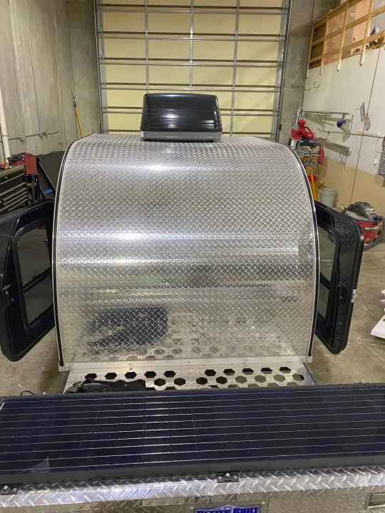 Front of an aluminum diamond plate RV rental trailer with rooftop vent and solar panel, parked in a garage.. TC Tear Drop TC Original 2022