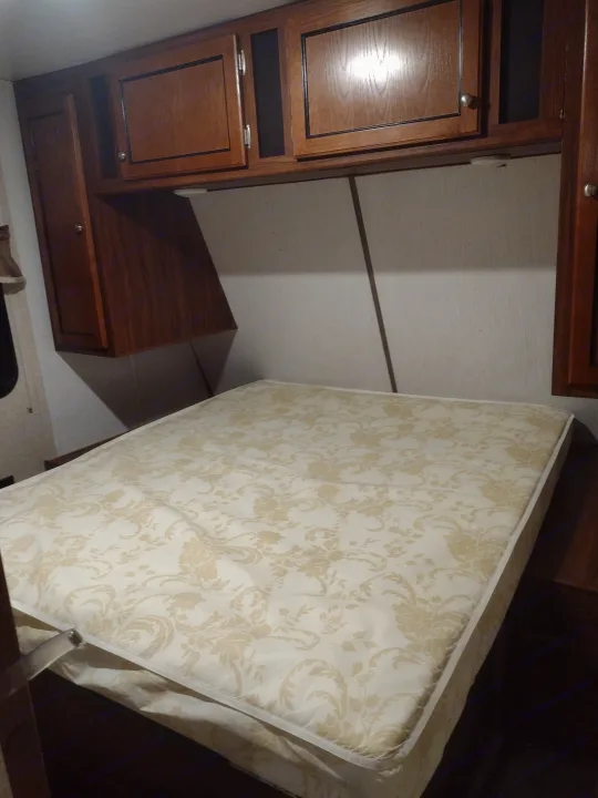 RV rental interior: lifted mattress for storage access, with wooden cabinets and compact design.. Heartland Trail Runner 2016
