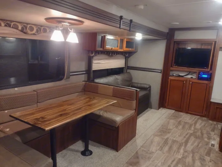 This RV rental's inviting interior features a dinette, leather sofa, TV, and cabinets. Ideal for travel!. Heartland Trail Runner 2016