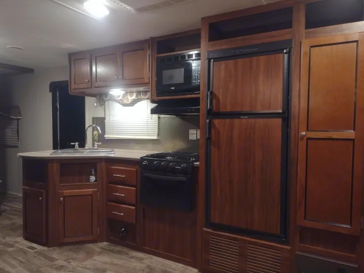 RV rental kitchen interior: modern wood cabinets, sink, microwave, fridge, and stove.. Heartland Trail Runner 2016