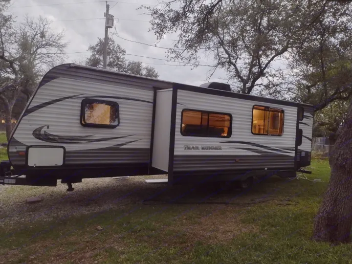 RV rental: A parked Trail Runner travel trailer with interior lights on and slide-out extended, set in a grassy area at dusk.. Heartland Trail Runner 2016