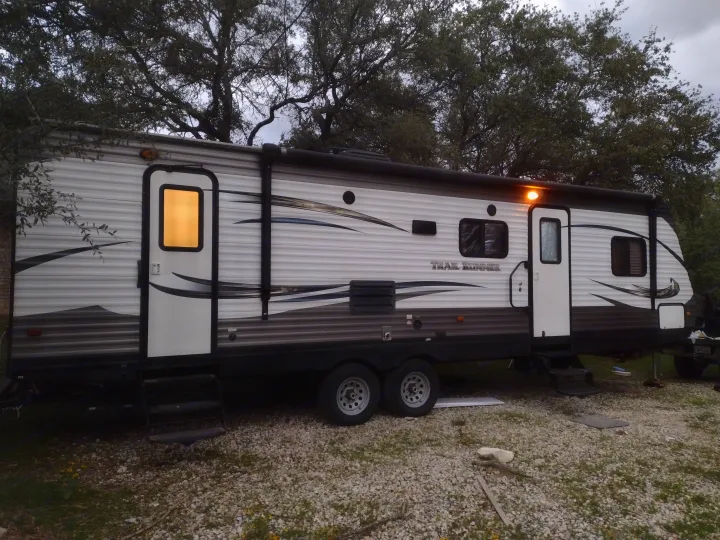 Spacious Trail Runner RV rental, a white and grey travel trailer with lights on, parked on a gravel lot.. Heartland Trail Runner 2016