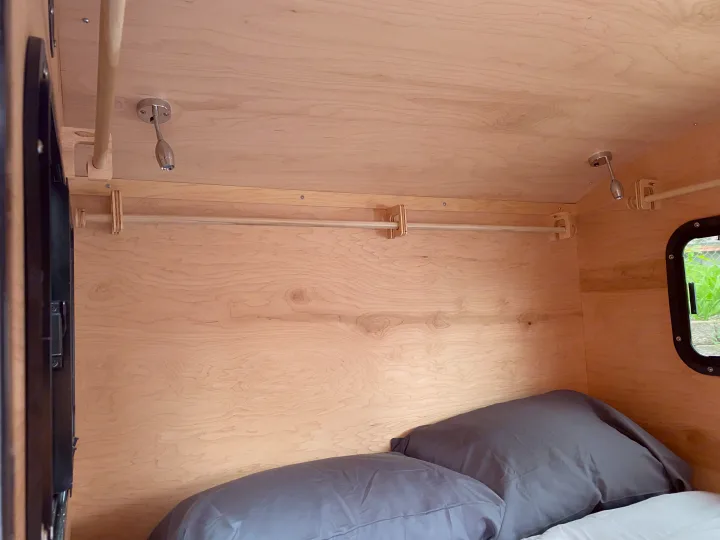 Cozy RV rental interior with light wood walls, a comfy bed, hanging rod, and ceiling-mounted reading lights.. TC Tear Drop TC Original 2022