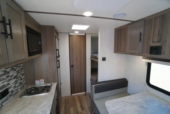 This RV rental interior features a functional kitchen with microwave & stove, a comfortable dinette, and a peek at bunk beds.. Gulf Stream Trailmaster 2022