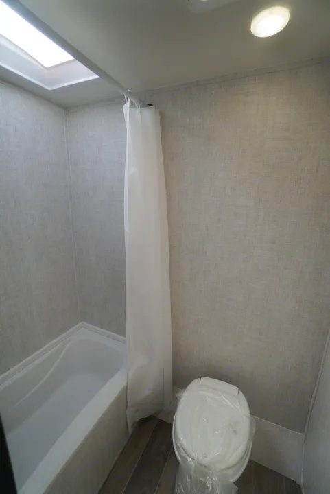 This RV rental bathroom features a tub/shower with curtain, a covered toilet, skylight, and light fixture, perfect for travelers.. Gulf Stream Trailmaster 2022