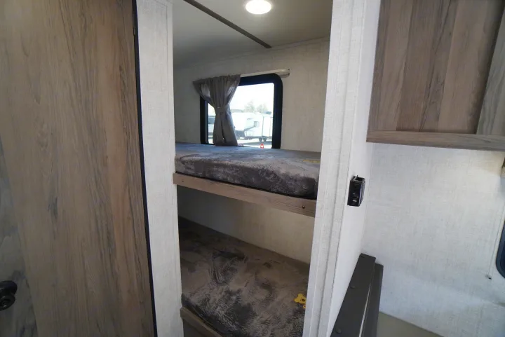 RV rental interior showing two stacked bunk beds with grey textured mattresses. Window, light, and power outlet visible.. Gulf Stream Trailmaster 2022