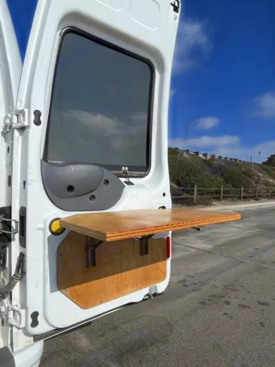 RV rental van's open door displays a convenient wooden fold-down table for outdoor use by the road.. Ford Transit 2012