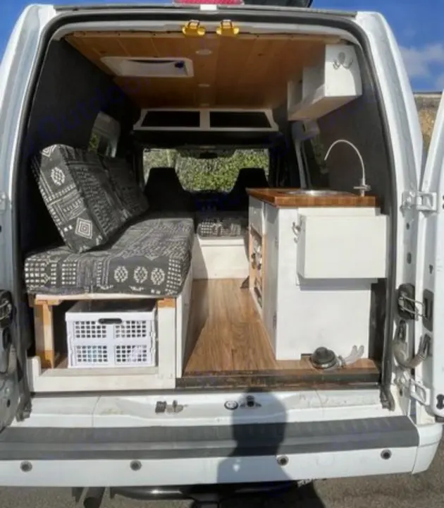 Explore this RV rental's cozy camper van interior: wood ceiling, patterned bed, and compact kitchen with sink, perfect for road trips.. Ford Transit 2012
