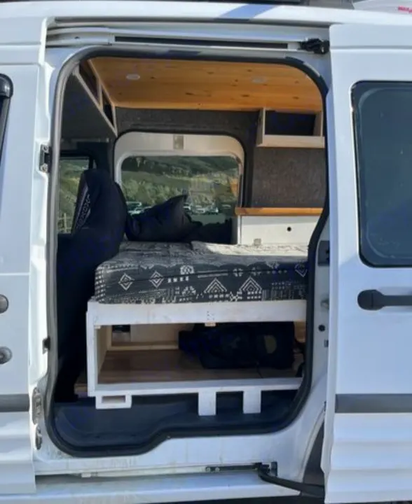 Inside a white, custom-built RV rental camper van: cozy bed, storage, wood accents. Ideal for mobile living & adventures.. Ford Transit 2012