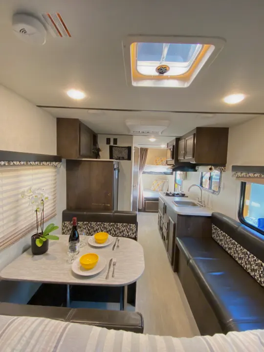 A bright RV rental interior showing a kitchen, a dining table set for two with wine and an orchid, and bunk beds.. Starcraft Launch 2018