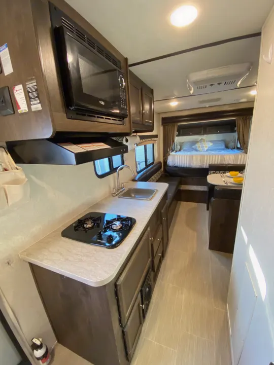 View of an RV rental's bright interior, showing kitchen with stove & microwave, dinette, and cozy bed area.. Starcraft Launch 2018