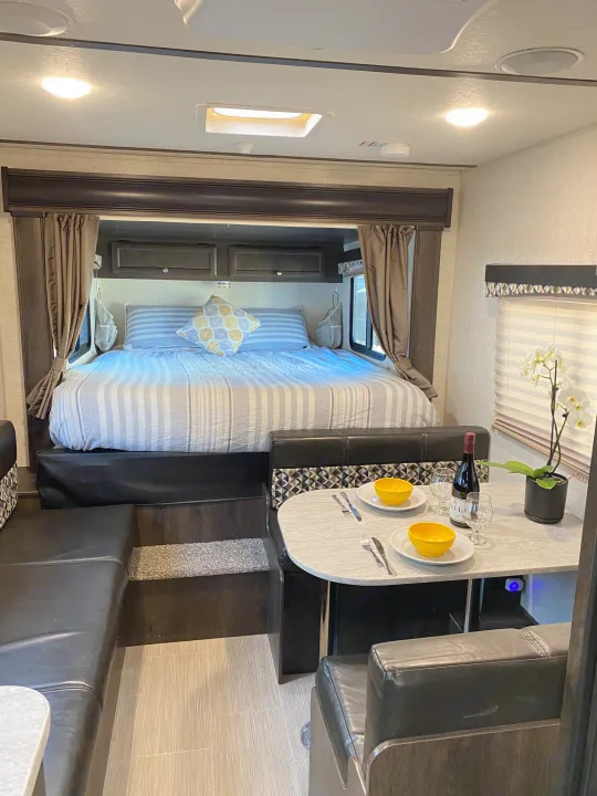 Inviting RV rental interior: cozy bed with striped bedding, and a comfortable dinette set for two with wine.. Starcraft Launch 2018