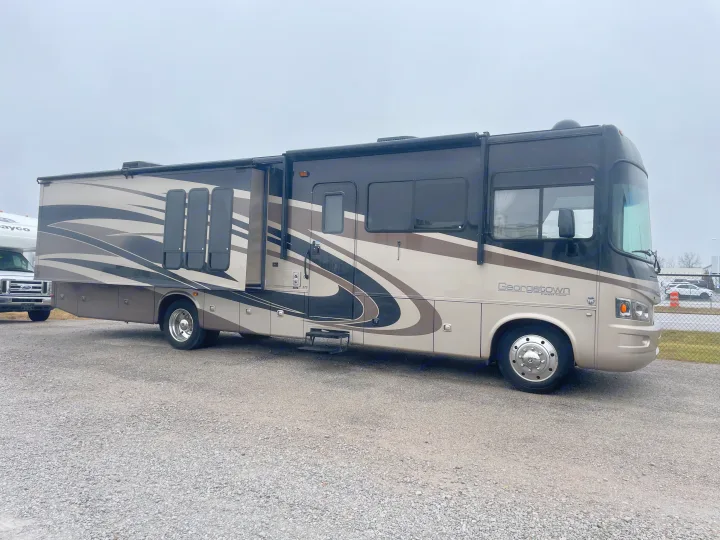 A large tan and black Georgetown motorhome with extended slide-outs is parked on a gravel lot, ready for RV rental.. Forest River Georgetown M373DS 2011