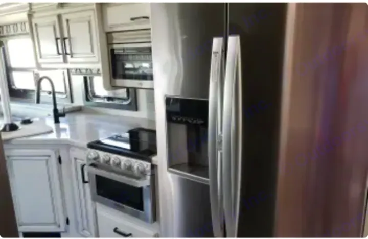 Modern RV rental kitchen interior: stainless steel fridge, stove, and sink with white cabinetry visible.. Jayco Precept 2020