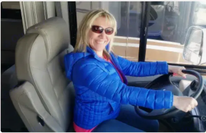 A smiling blonde woman in a blue jacket grips the steering wheel of an RV, ready for a fun RV rental trip.. Jayco Precept 2020