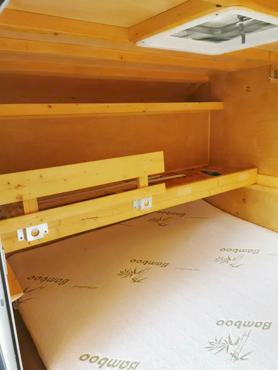 Wooden interior of an RV rental: shelves, bed platform, and ceiling vent visible for comfort.. Custom Built Custom Built 2021