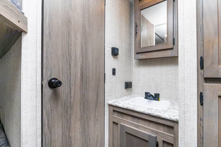 Inside an RV rental: a compact bathroom with a wooden door, sink, mirrored cabinet, and light textured walls.. Gulf Stream Kingsport 2022