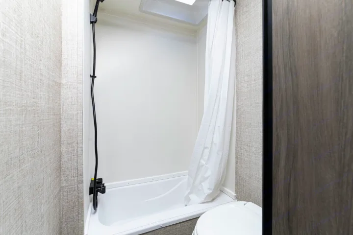 Explore this RV rental's compact bathroom, featuring a shower/tub with curtain, toilet, and light-textured walls.. Gulf Stream Kingsport 2022