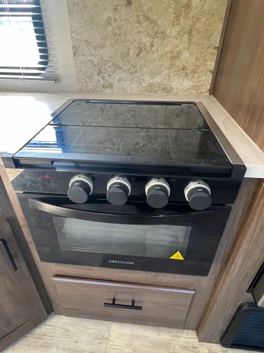 RV rental kitchen with a GreyStone oven and stovetop. The range features control knobs and a reflective glass cooktop cover.. Avenger Avenger Trailer 2021
