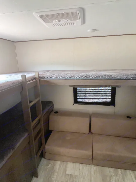 An RV rental interior showing a bunk bed setup with ladder, a convertible sofa, and ceiling AC. Comfortable family space.. Avenger Avenger Trailer 2021