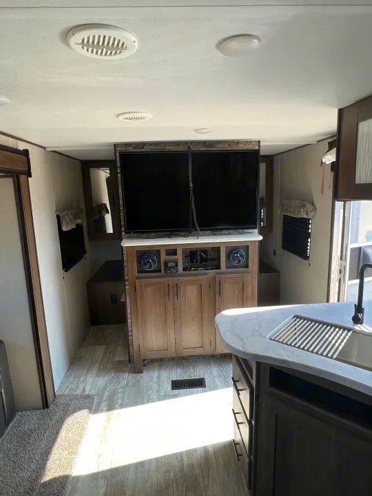 Bright RV rental interior with a large TV entertainment center, detailed built-ins, and a functional kitchen island.. Avenger Avenger Trailer 2021