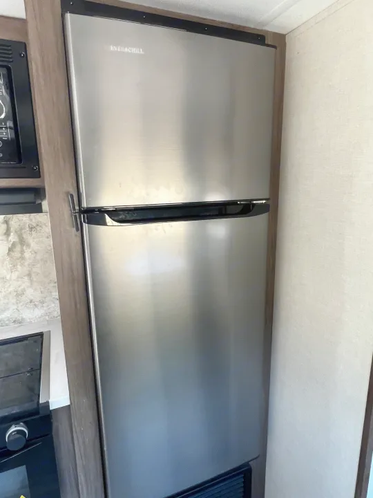 RV rental's Ever Chill stainless steel refrigerator/freezer, with microwave, in a compact camper kitchen.. Avenger Avenger Trailer 2021