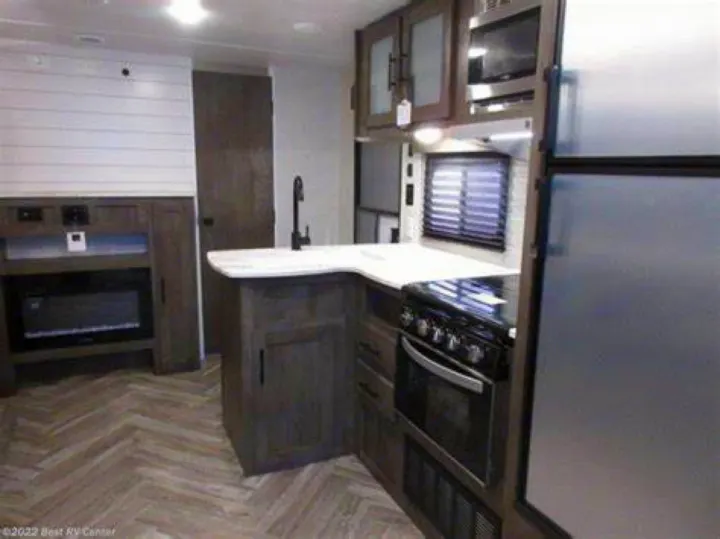 Inside a well-appointed rv rental: modern kitchen with stove, microwave, sink, ample cabinets, plus an electric fireplace.. Forest River Wildwood X-Lite 2022