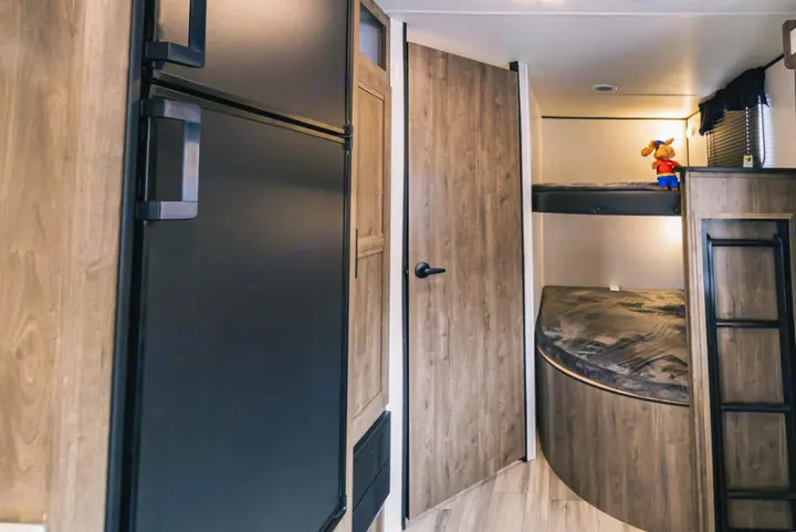 RV rental interior: modern black fridge, wooden door, bunk beds with ladder, & curved lower bed.. Heartland Pioneer 2022