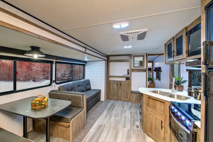 Step inside this RV rental! A warm interior with a kitchen, dining booth, and sofa offers cozy comfort and snowy outdoor views.. Heartland Pioneer 2022