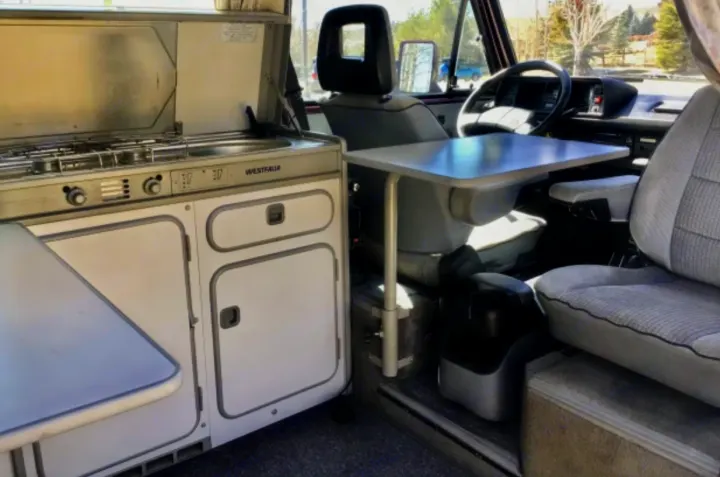 Interior of an RV rental camper van showing a Westfalia kitchen (stove/sink), adjustable table, and front seats.. Volkswagen Westfalia 1990