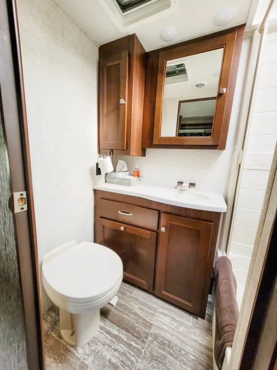 Clean RV rental bathroom featuring a toilet, wood vanity with sink, mirrored cabinet, and shower area. Compact and functional.. Forest River Sunseeker LE 2018