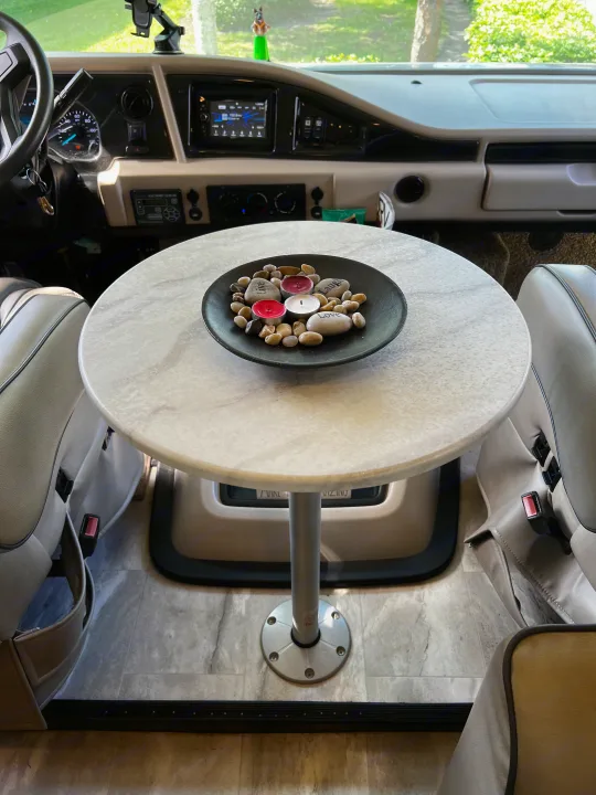RV rental interior: Swivel chairs pulled to a round table, facing the dashboard. View of green trees through the windshield.. Holiday Rambler Admiral 2021