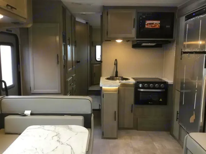 Modern RV rental interior featuring a compact kitchen with sink, stove, microwave, fridge, and a cozy dinette seating.. Forest River Coachmen Freelander Premier 2022