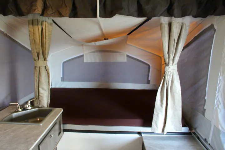 RV rental pop-up camper interior: features a bed, sink, and tied-back curtains, offering a functional camping space.. Forest River Rockwood ESP 2021