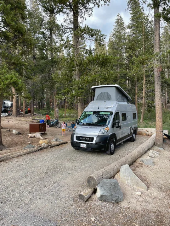 RV rental camping: Silver Winnebago camper van at a rustic site with people & bikes.. Winnebago Solis 2022