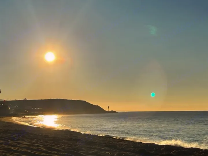 Golden light from a sunset bathes a beach, ocean, and coastal hill, with sun glare on the water. Ideal for an rv rental getaway.. Forest River Rockwood Geo Pro 2023
