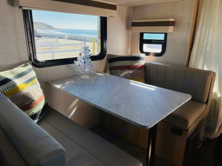 RV rental dinette with ocean view. The cozy camper interior features a small white Christmas tree, overlooking a beach.. Forest River Rockwood Geo Pro 2023