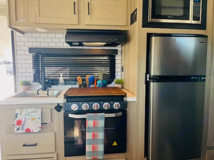 This modern RV rental kitchen features a microwave, refrigerator, stove/oven, sink, and subway tile backsplash.. Forest River Rockwood Geo Pro 2023