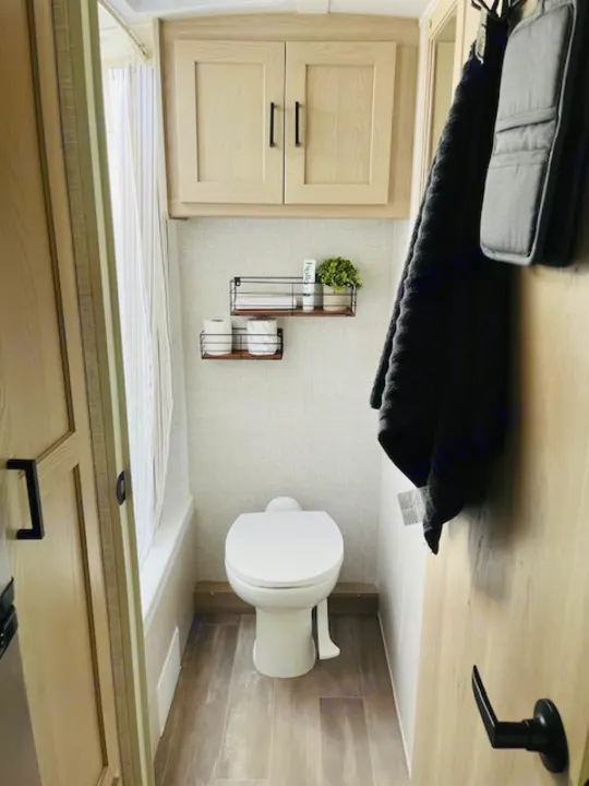 Modern RV rental bathroom showcasing a toilet, practical wall shelves, and light wood cabinetry. Efficient and clean design.. Forest River Rockwood Geo Pro 2023