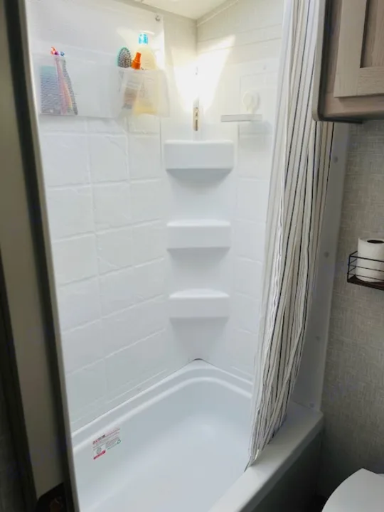 Clean RV rental bathroom: compact white shower/tub, built-in shelves, and a hanging organizer for toiletries.. Forest River Rockwood Geo Pro 2023