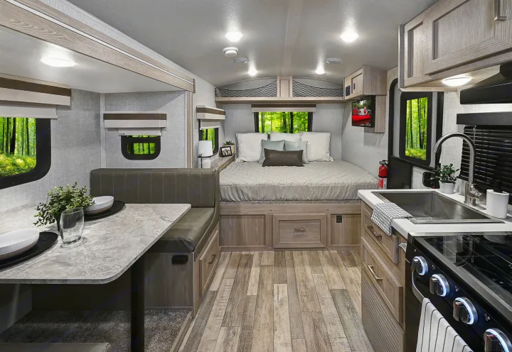 Explore this cozy RV rental interior, complete with a dinette, bed, and kitchen, surrounded by nature.. Forest River Rockwood Geo Pro 2023