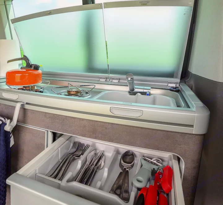 RV rental's compact kitchen: gas stove, sink, and a pull-out drawer with utensils for convenient camping.. Volkswagen California Ocean 2024