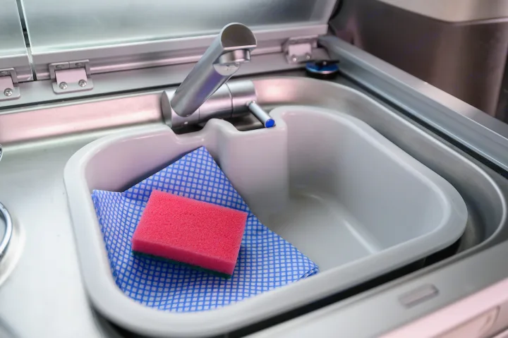 Compact RV rental kitchen sink, featuring a faucet, pink sponge, and blue cloth for easy clean-up on the go.. Volkswagen California Ocean 2024