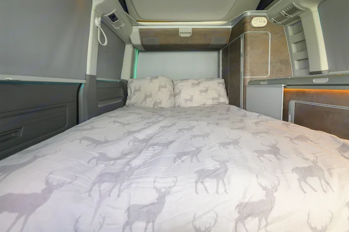 Spacious rv rental interior featuring a large bed with deer print duvet, compact fridge, and window blinds.. Volkswagen California Ocean 2024