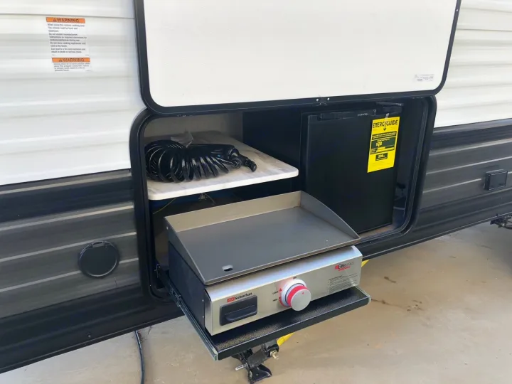 This rv rental features a convenient outdoor kitchen with a pull-out griddle, mini-fridge, and hose, ideal for camping and cooking.. Forest River Wildwood 2020